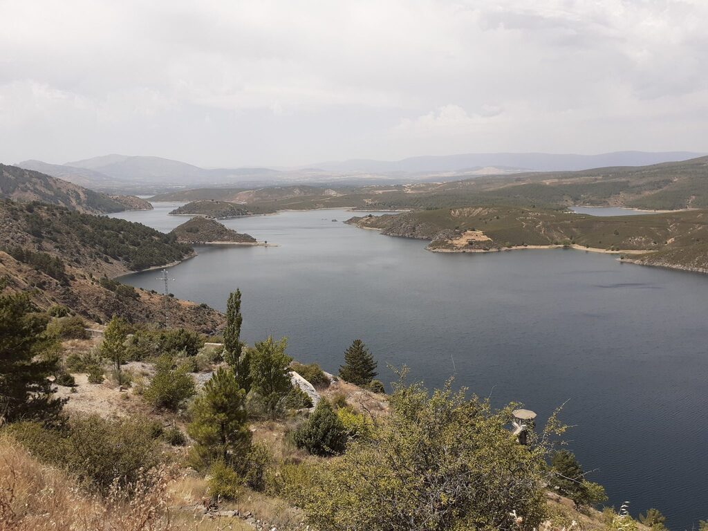 Lago visto desde una perspectiva elevada, rodeado de montañas y vegetación.