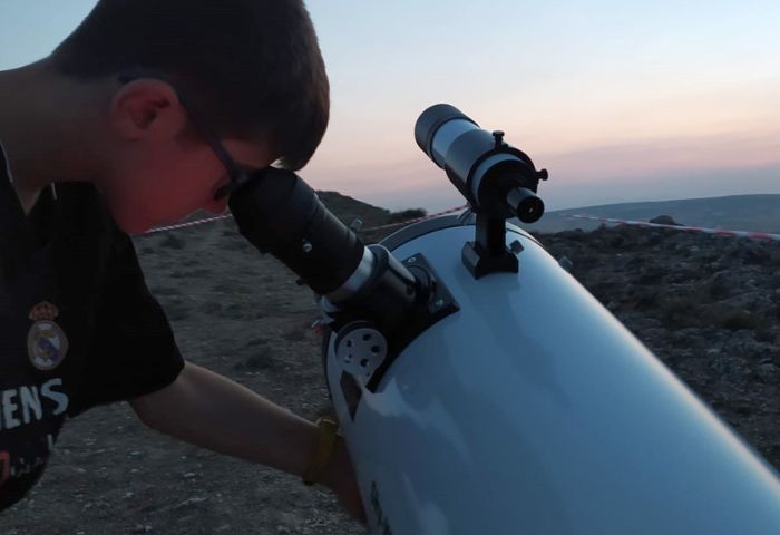 Niño observando a través de un telescopio durante el atardecer en una sesión de astronomía.