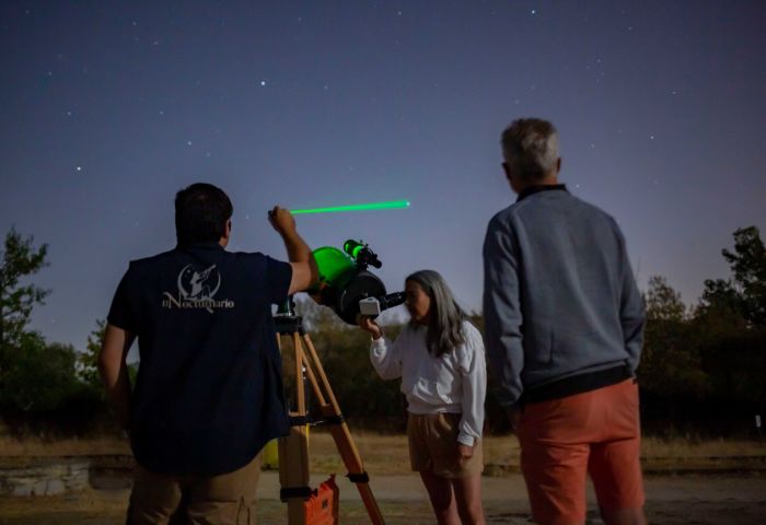 Grupo de personas realizando observación astronómica con telescopio y puntero láser bajo un cielo estrellado.