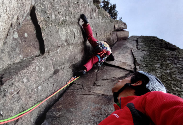 Guía de escalada asistiendo a un escalador en una pared rocosa.